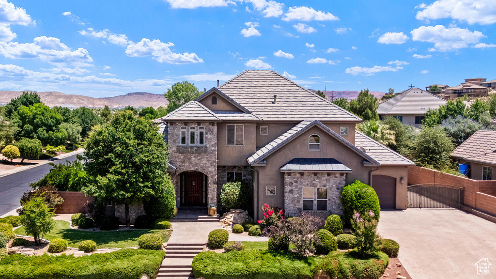 View of front of house with stone siding, stucco siding, concrete driveway, a mountain view, and a gate