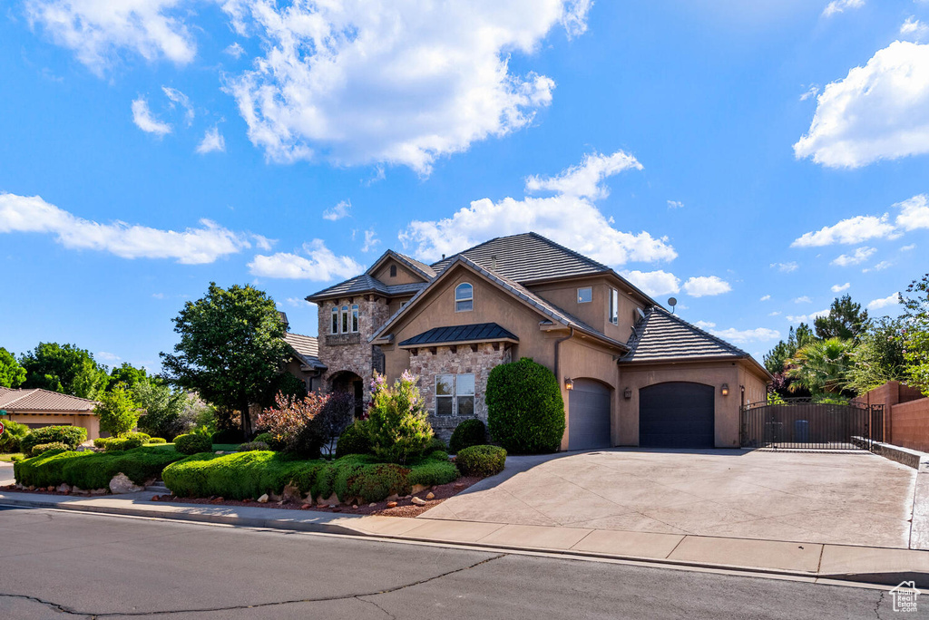 View of front facade with stucco siding, a garage, stone siding, driveway, and a tile roof