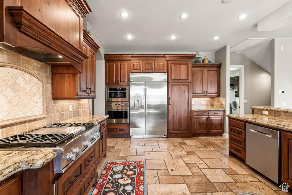Kitchen with stainless steel appliances, washer / dryer, custom range hood, recessed lighting, and stone tile floors