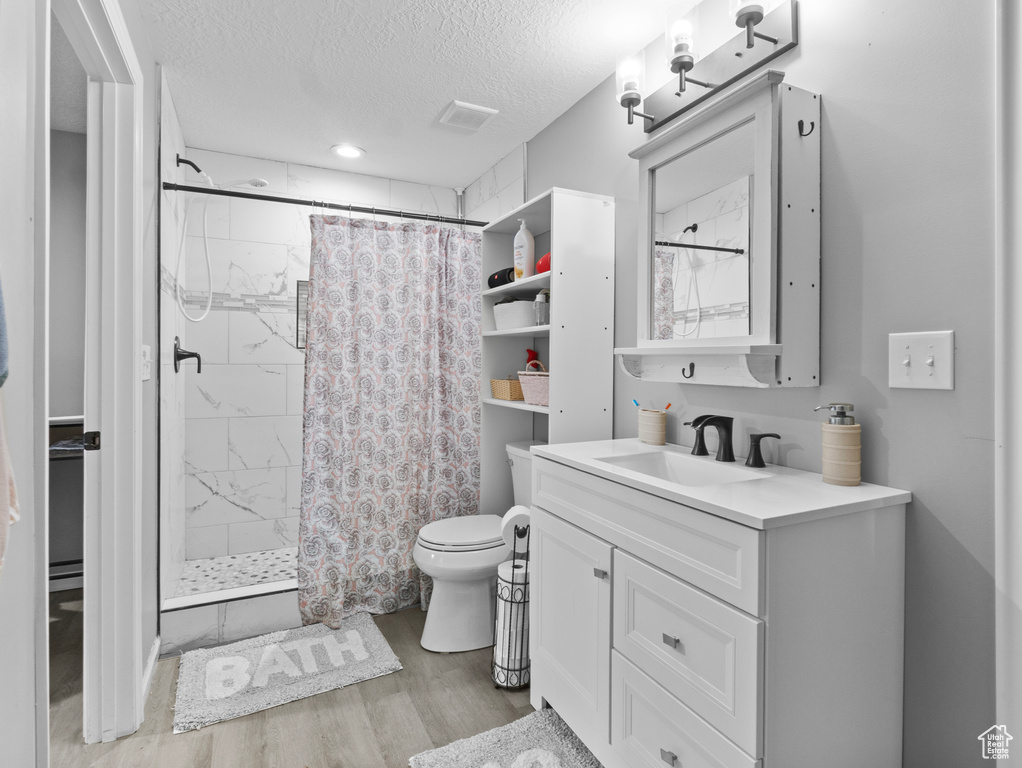 Full bath with a stall shower, vanity, wood finished floors, and a textured ceiling