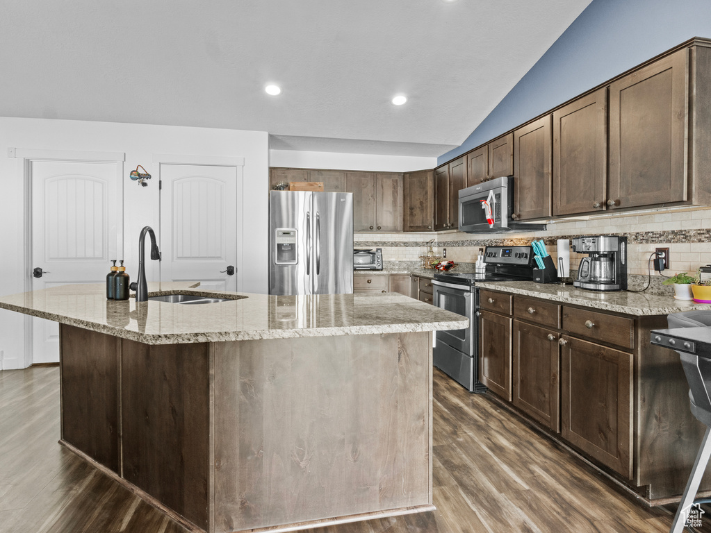 Kitchen featuring appliances with stainless steel finishes, dark wood finished floors, decorative backsplash, light stone countertops, and vaulted ceiling