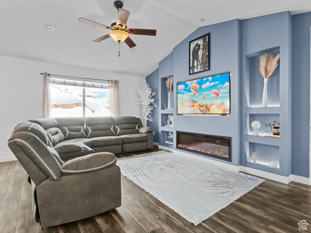 Living room featuring a ceiling fan, dark wood-style floors, lofted ceiling, and a glass covered fireplace