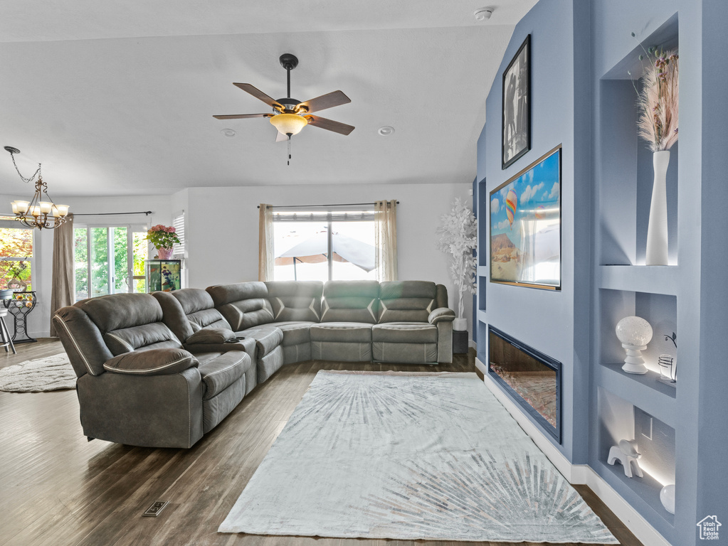Living area with dark wood-type flooring, a chandelier, ceiling fan, and a glass covered fireplace