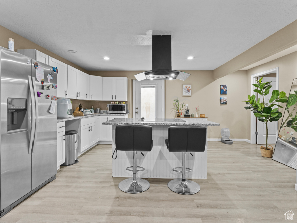 Kitchen featuring appliances with stainless steel finishes, island range hood, a kitchen island, white cabinetry, and a breakfast bar area