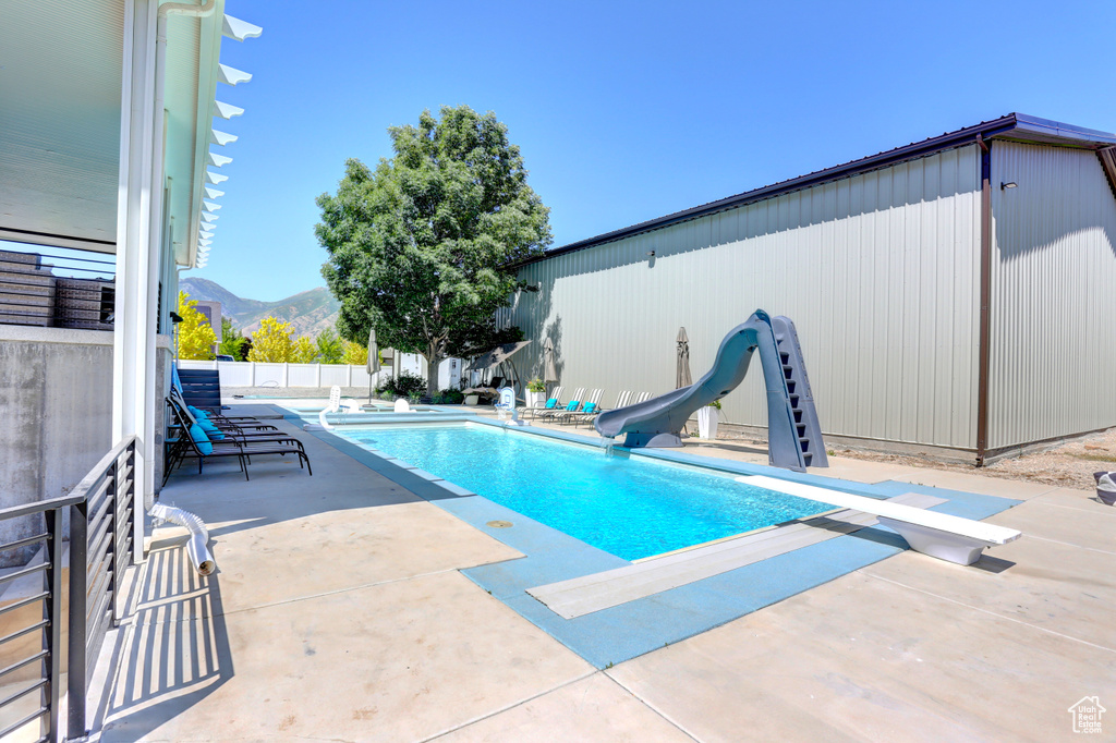 View of swimming pool with a water slide, a diving board, a patio, and a mountain view