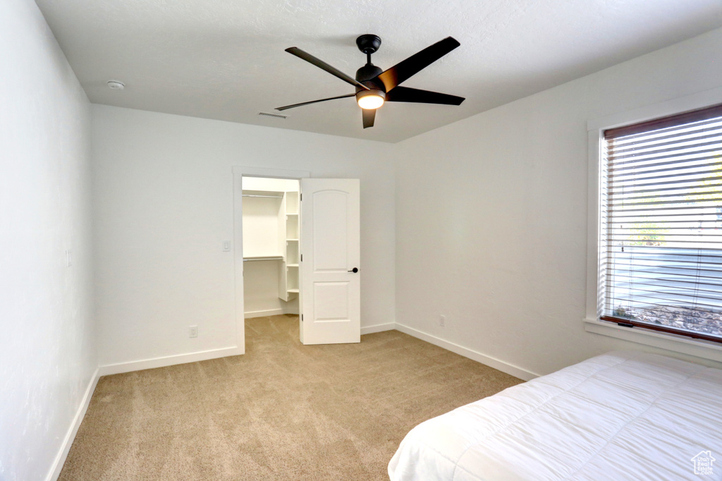 Bedroom featuring light colored carpet, a spacious closet, a ceiling fan, and a closet