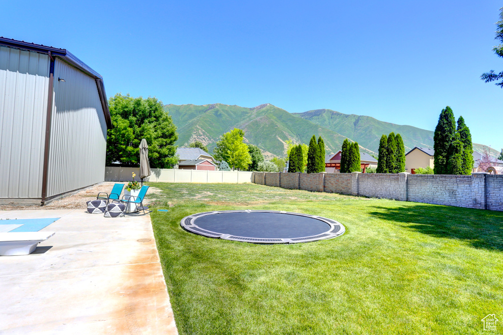 Fenced backyard with a trampoline, a mountain view, and a patio