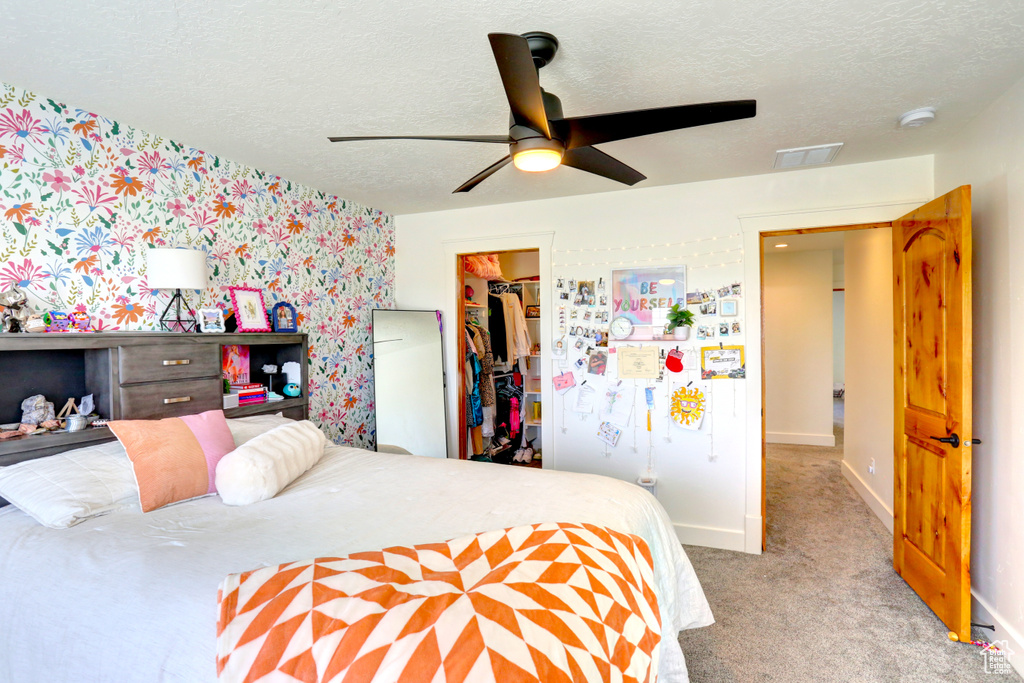 Bedroom featuring wallpapered walls, a spacious closet, carpet flooring, a textured ceiling, and a closet