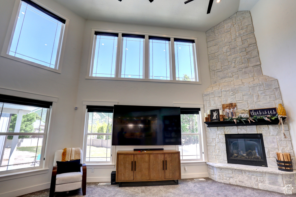 Living area with ceiling fan, plenty of natural light, a fireplace, carpet flooring, and a towering ceiling