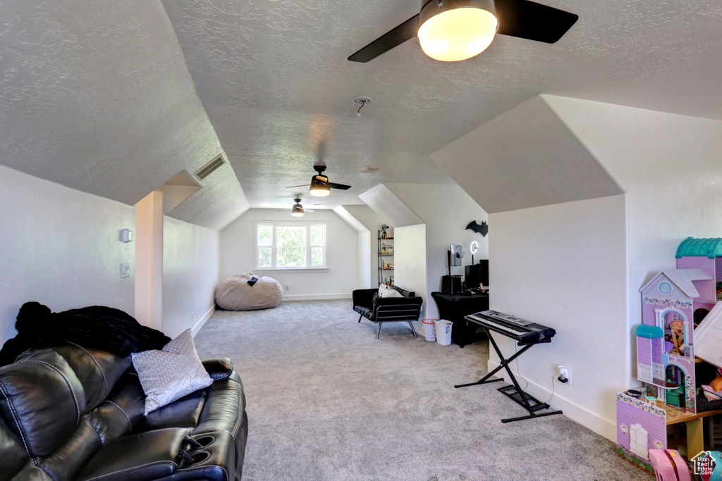 Interior space with ceiling fan, a textured ceiling, carpet floors, and vaulted ceiling