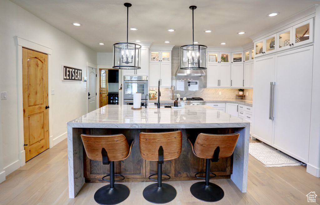 Kitchen featuring paneled refrigerator, light wood finished floors, tasteful backsplash, white cabinets, and recessed lighting