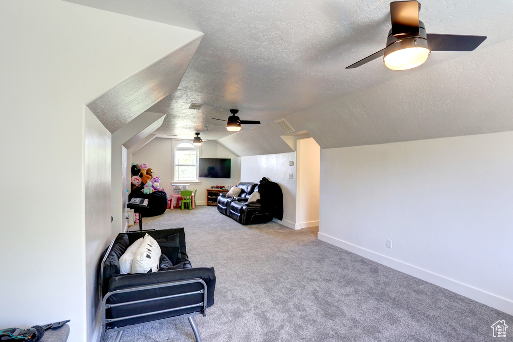Living area with ceiling fan, a textured ceiling, lofted ceiling, and carpet