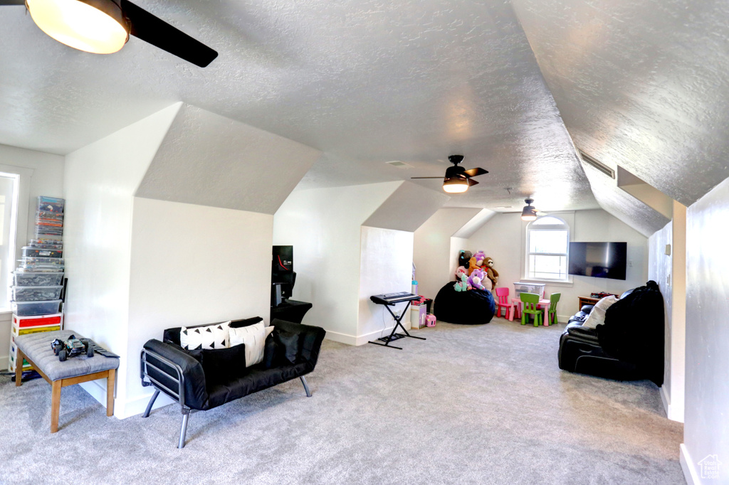 Living area with ceiling fan, a textured ceiling, carpet, and vaulted ceiling