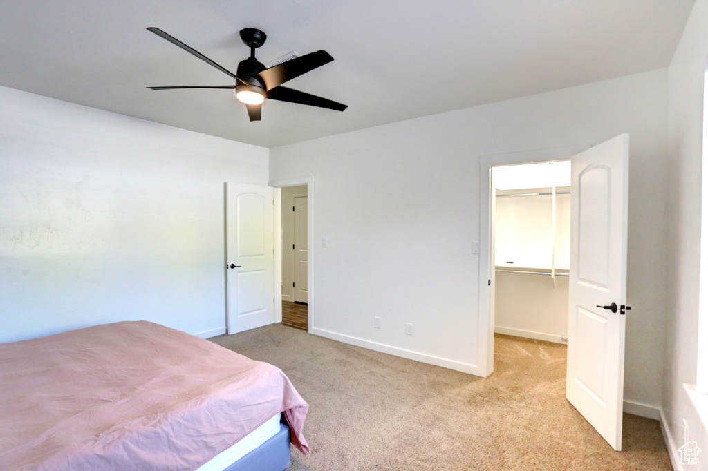 Bedroom with light carpet, a spacious closet, and a ceiling fan
