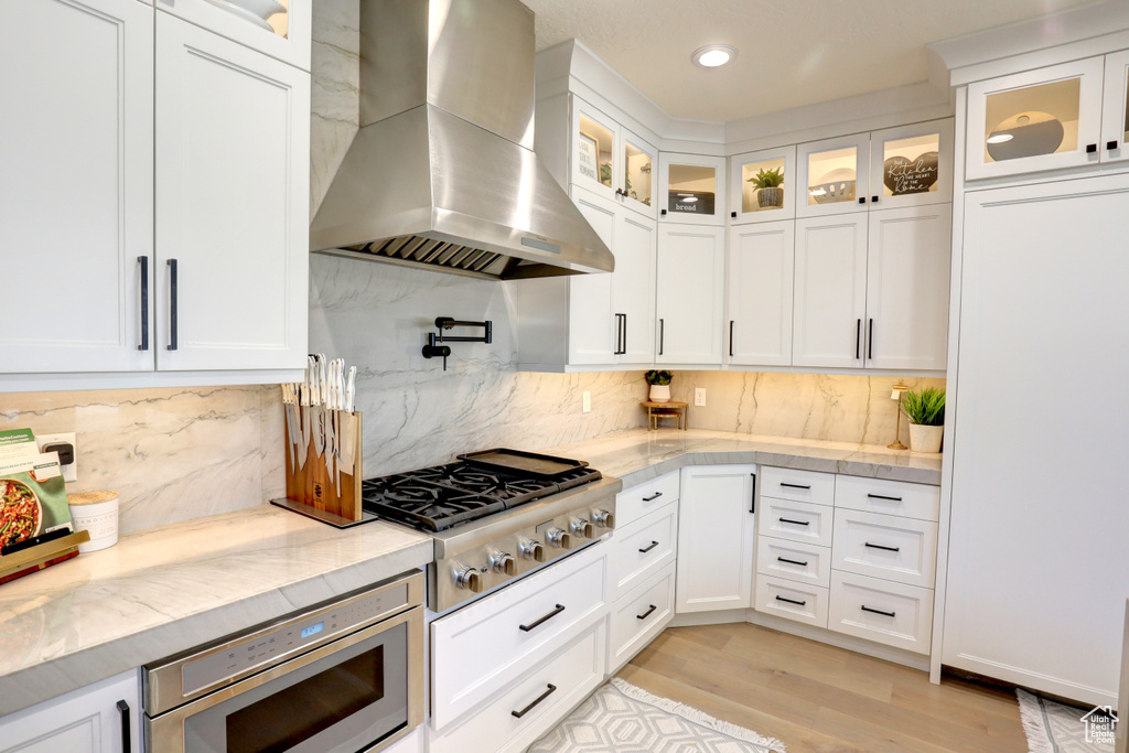 Kitchen featuring exhaust hood, stainless steel appliances, white cabinetry, light wood-style flooring, and recessed lighting