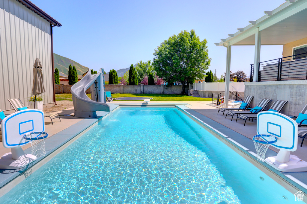 View of pool featuring a water slide, a patio, a fenced backyard, and a mountain view