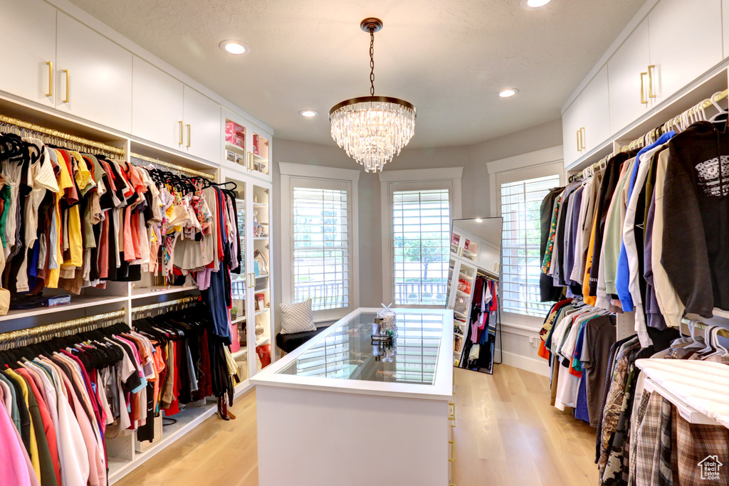 Walk in closet with light wood finished floors and a chandelier