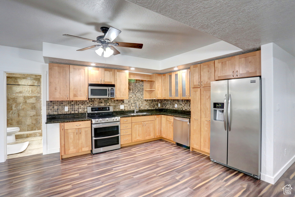 Kitchen featuring stainless steel appliances, light brown cabinets, dark countertops, ceiling fan, and a textured ceiling