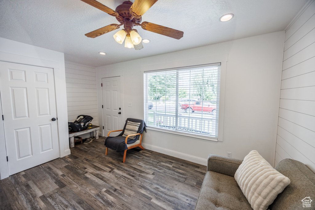 Living area with dark wood-style floors, ceiling fan, recessed lighting, and wood walls