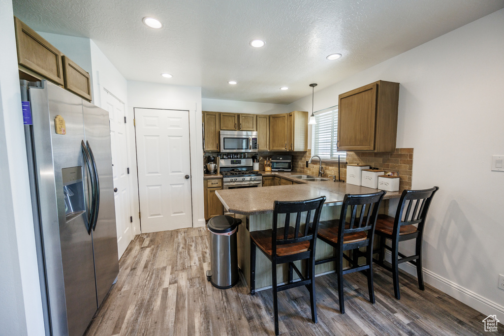 Kitchen featuring stainless steel appliances, a peninsula, wood finished floors, backsplash, and recessed lighting