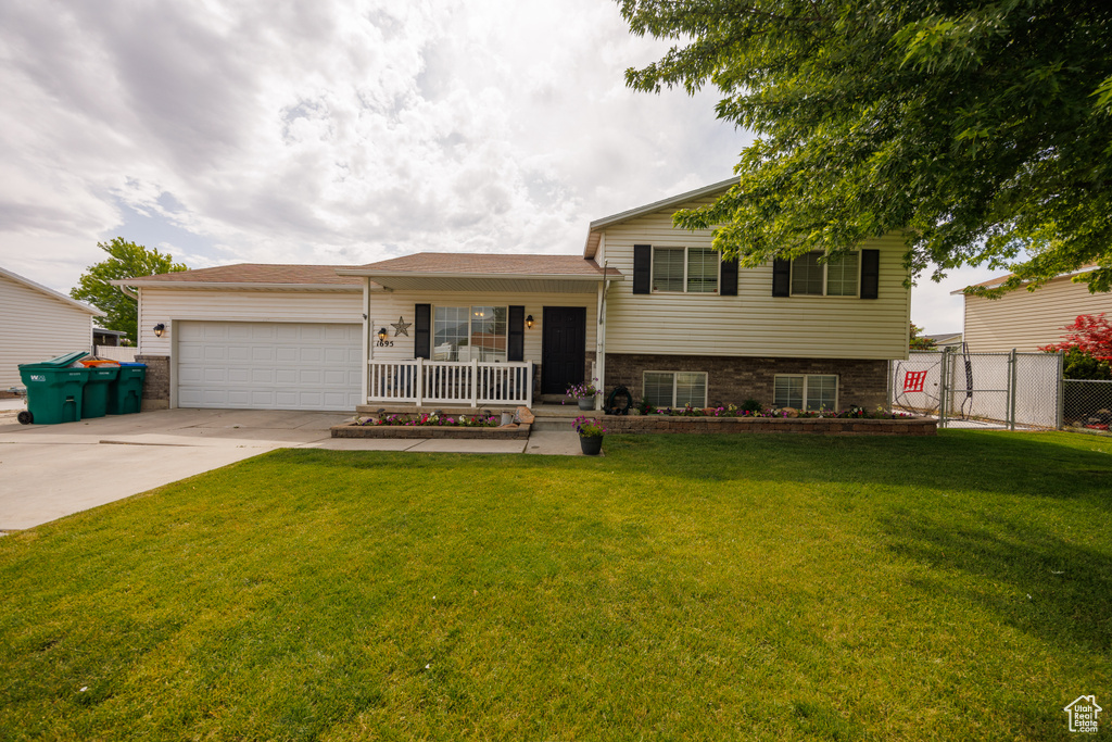 Split level home with a porch, driveway, an attached garage, and a gate