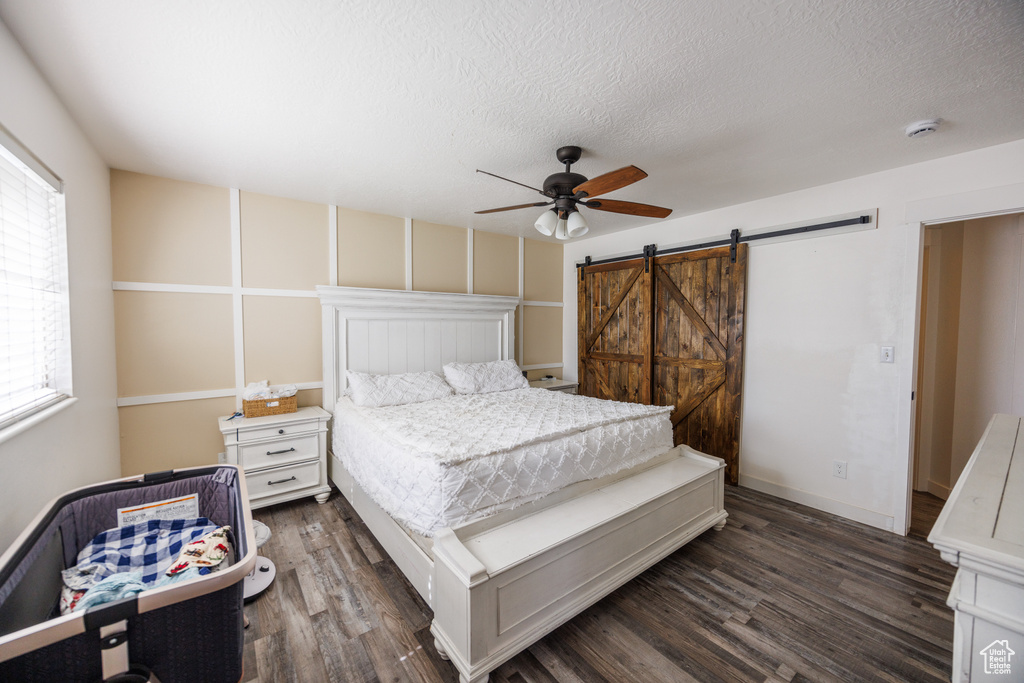 Bedroom featuring dark wood-type flooring, a barn door, a ceiling fan, and a textured ceiling