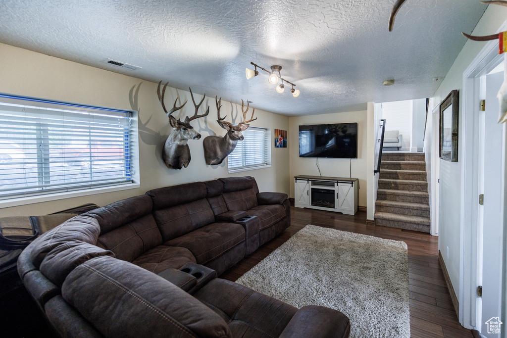 Living room with a textured ceiling, dark wood-style floors, and stairs