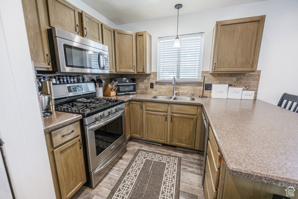 Kitchen with stainless steel appliances, a peninsula, backsplash, and light wood-style flooring