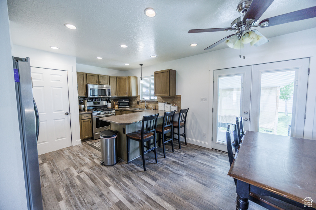 Kitchen with appliances with stainless steel finishes, a peninsula, wood finished floors, recessed lighting, and a breakfast bar area