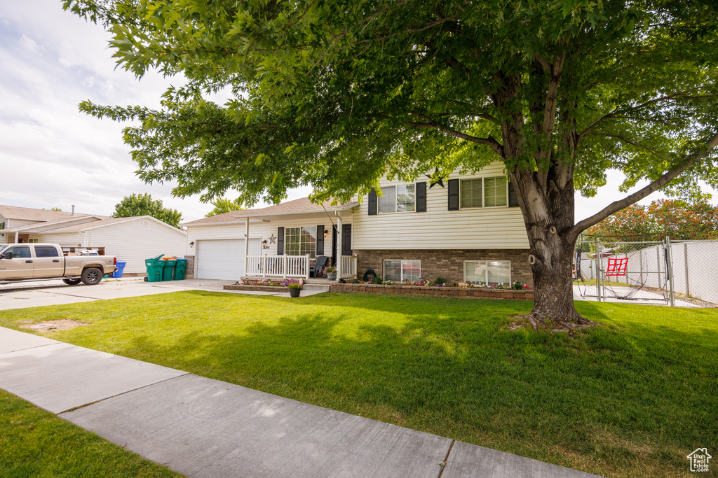 Split level home with concrete driveway, a garage, covered porch, and brick siding