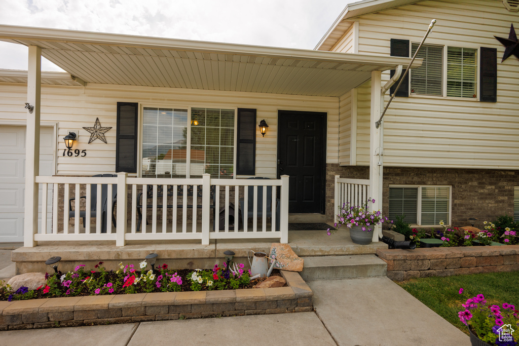 Entrance to property with covered porch, brick siding, and an attached garage