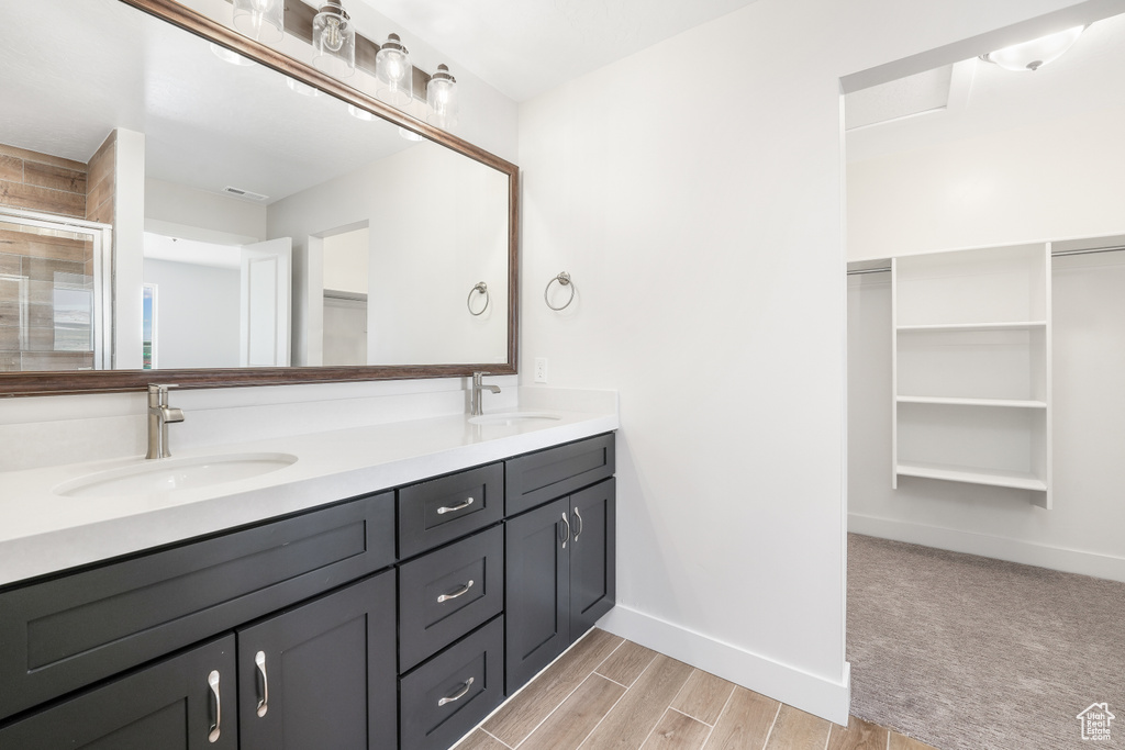 Bathroom with double vanity, a spacious closet, a stall shower, and wood finished floors