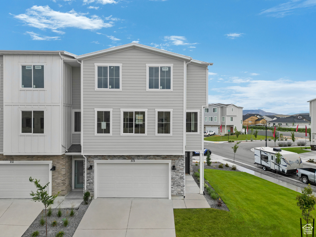Townhome / multi-family property featuring a garage, concrete driveway, stone siding, a front lawn, and board and batten siding