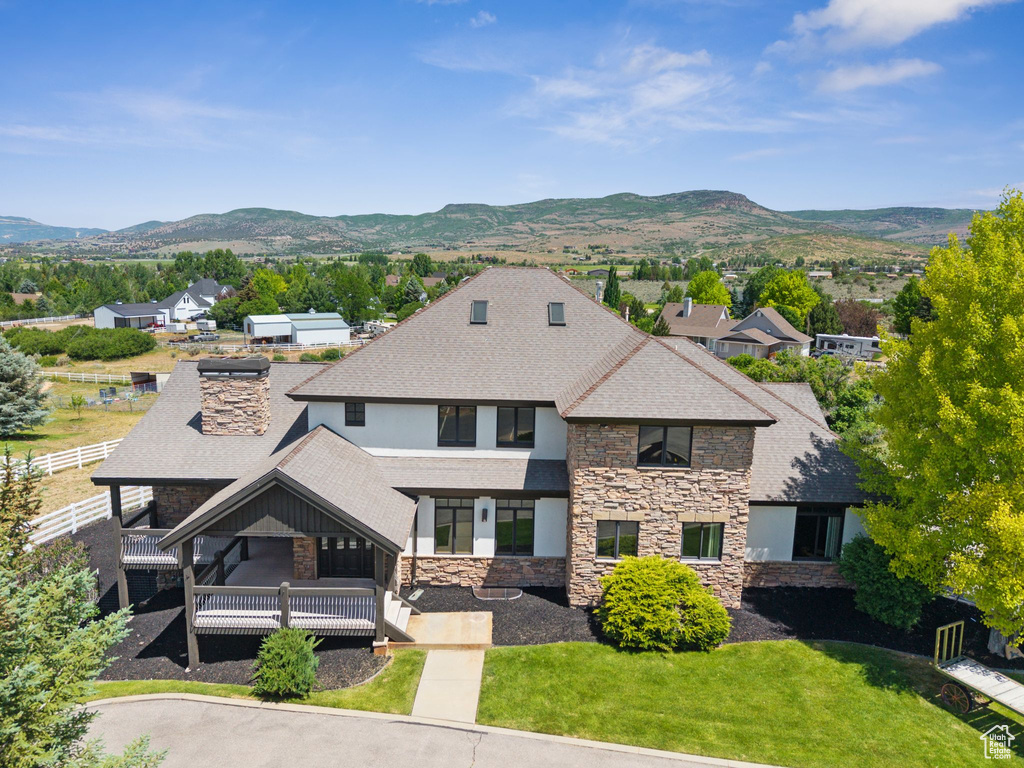 View of front of property with stone siding, roof with shingles, a mountain view, and a balcony