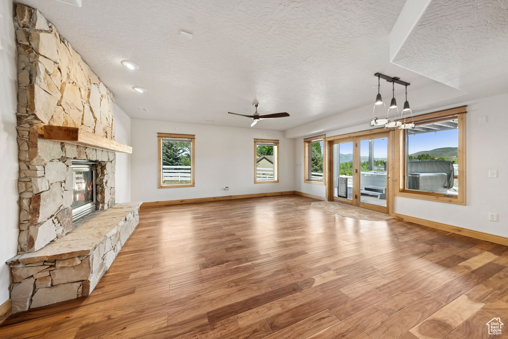 Unfurnished living room featuring a textured ceiling, a stone fireplace, light wood-type flooring, and ceiling fan
