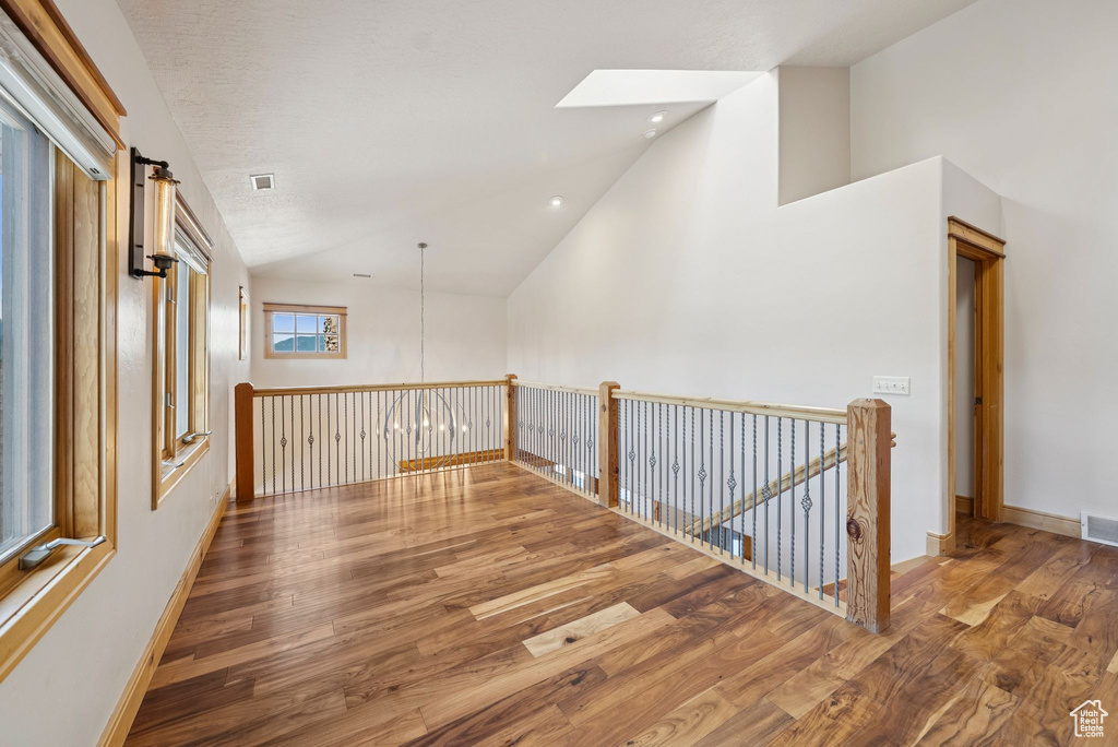 Corridor with wood finished floors, a skylight, recessed lighting, an upstairs landing, and high vaulted ceiling