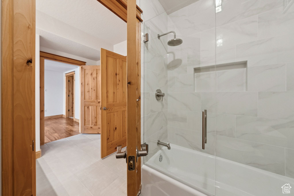Full bath with combined bath / shower with glass door and tile patterned floors