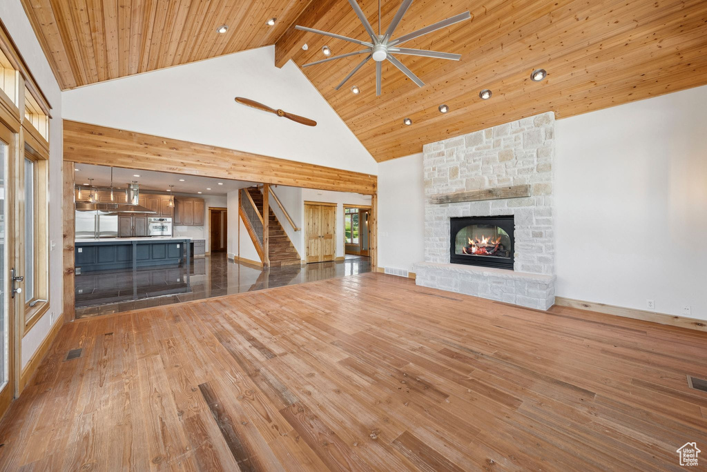 Unfurnished living room with stairway, high vaulted ceiling, ceiling fan, hardwood / wood-style floors, and a stone fireplace