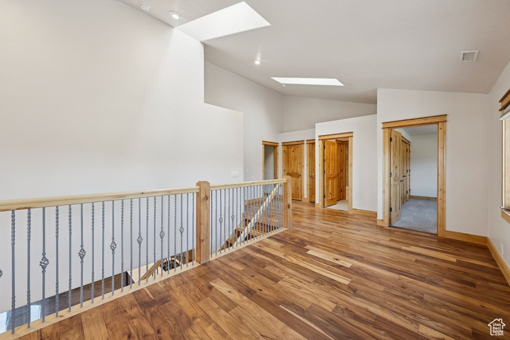 Corridor featuring a skylight, lofted ceiling, wood finished floors, and an upstairs landing