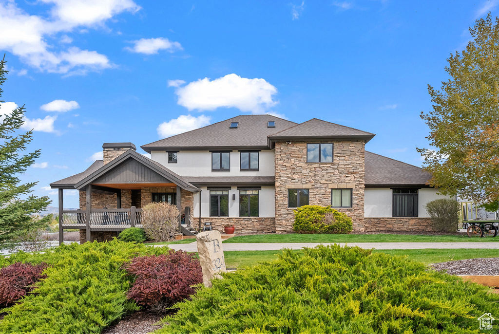 View of front of home with stone siding, stucco siding, a chimney, and roof with shingles