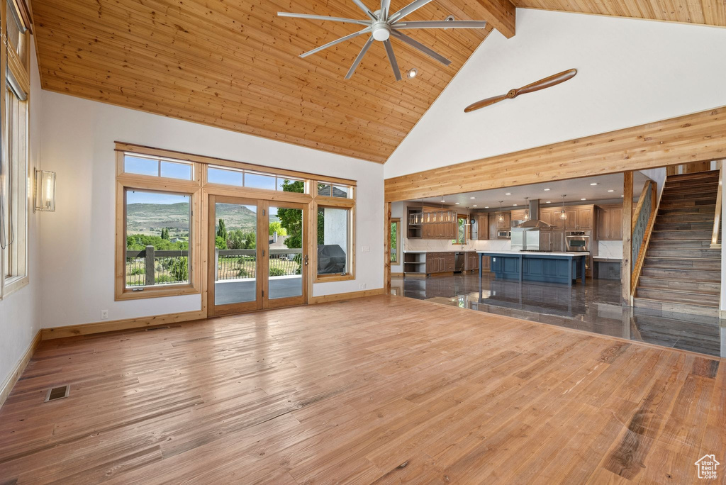 Unfurnished living room featuring high vaulted ceiling, a ceiling fan, wood finished floors, stairway, and a wood ceiling with exposed beams