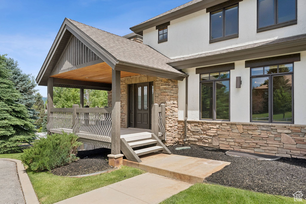 View of front of home with stone siding, stucco siding, a shingled roof, and covered porch