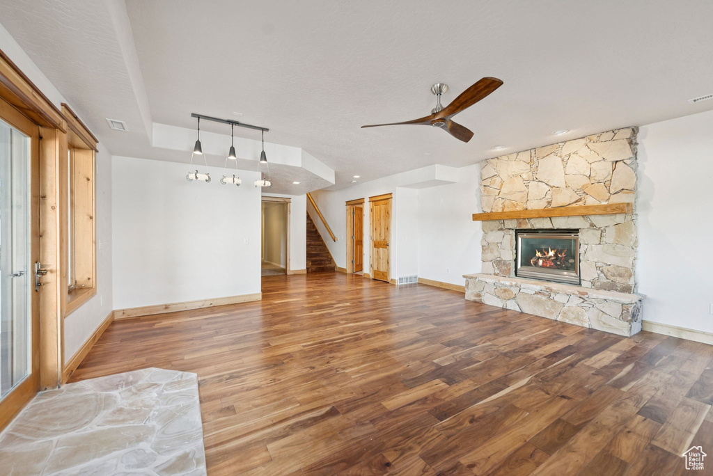 Unfurnished living room with stairs, wood finished floors, a stone fireplace, and a ceiling fan