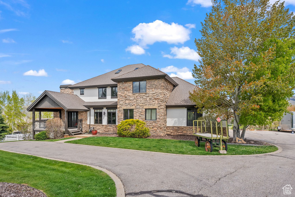 View of front facade with stone siding, a shingled roof, a front yard, and stucco siding