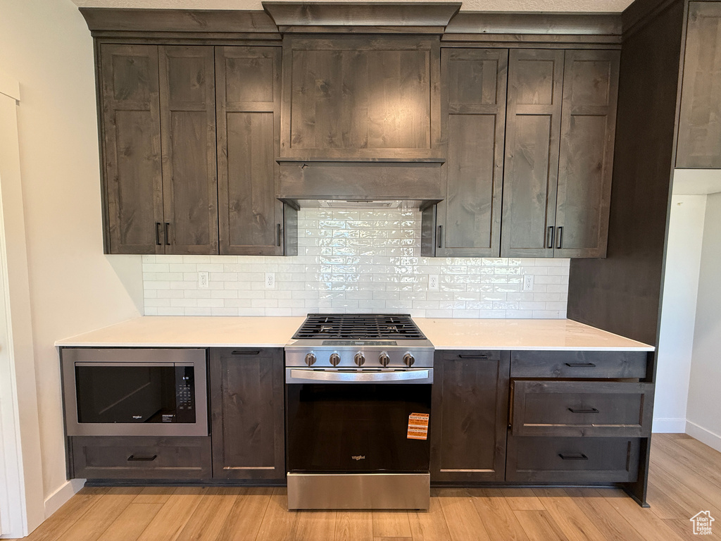 Kitchen featuring appliances with stainless steel finishes, light wood finished floors, dark brown cabinetry, and light countertops