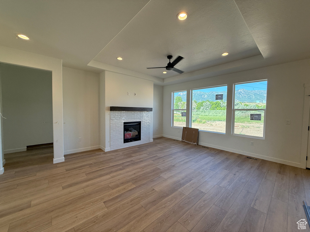 Unfurnished living room with a raised ceiling, light wood-type flooring, a fireplace, a ceiling fan, and recessed lighting
