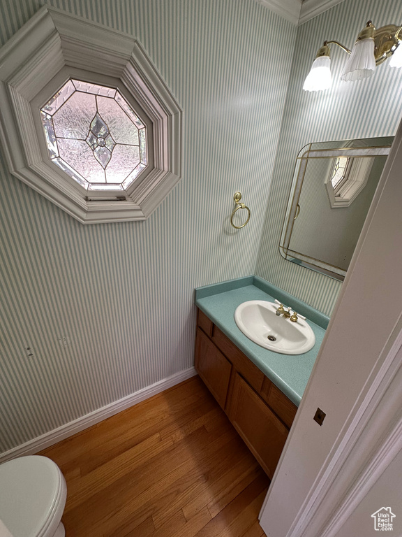 Half bath featuring wood finished floors, wallpapered walls, and vanity