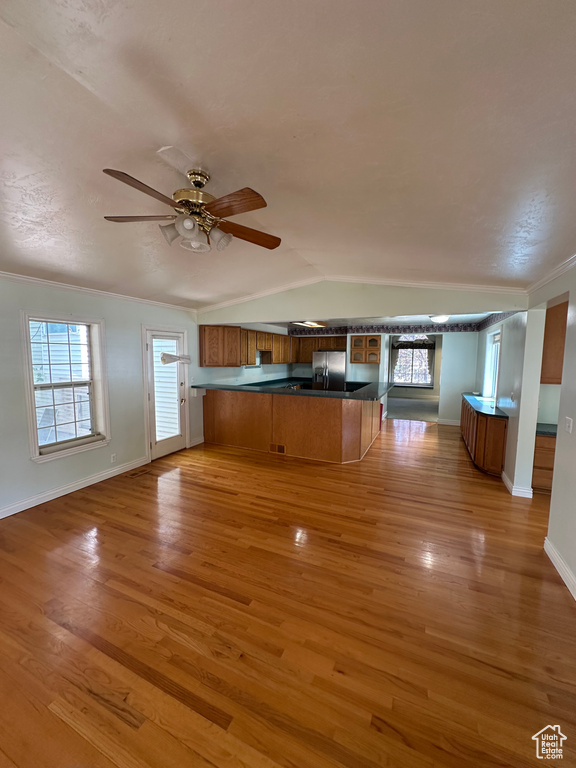 Kitchen with stainless steel fridge, open floor plan, brown cabinets, a peninsula, and dark countertops