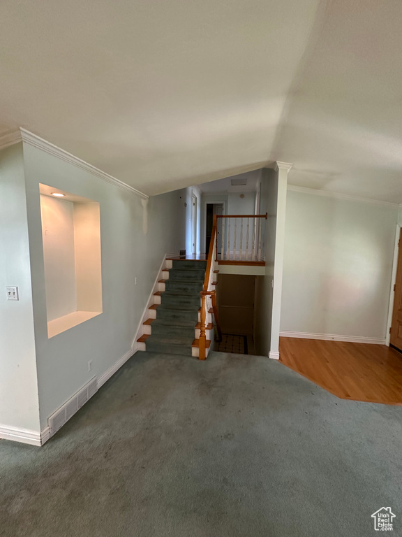 Unfurnished living room with stairs, carpet flooring, ornamental molding, and lofted ceiling