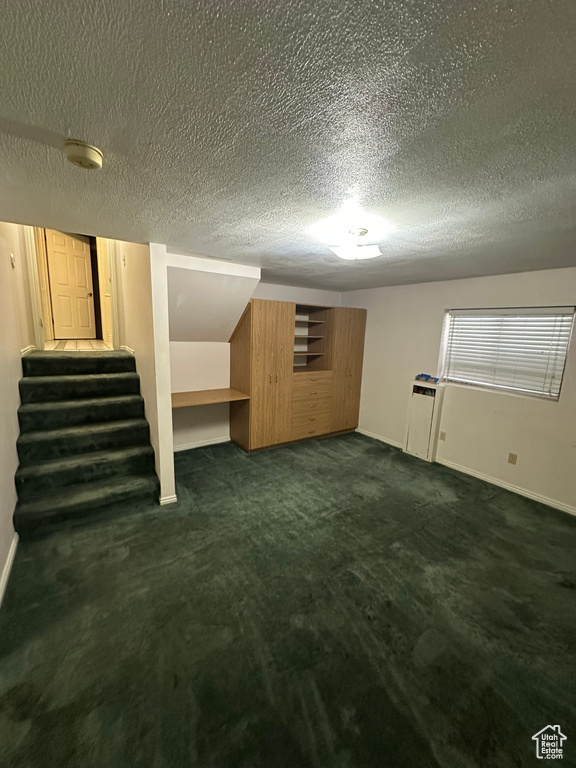 Finished basement featuring stairway, dark colored carpet, and a textured ceiling
